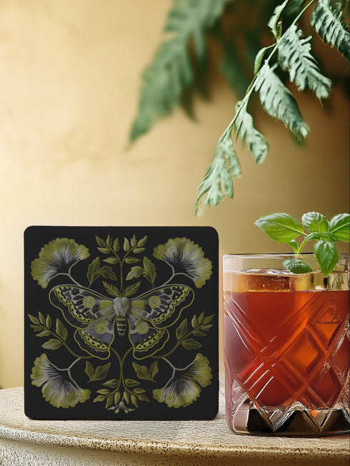 Square black ceramic coaster featuring a detailed chartreuse luna moth illustration surrounded by symmetrical botanical elements including ginkgo-inspired leaves and delicate foliage.